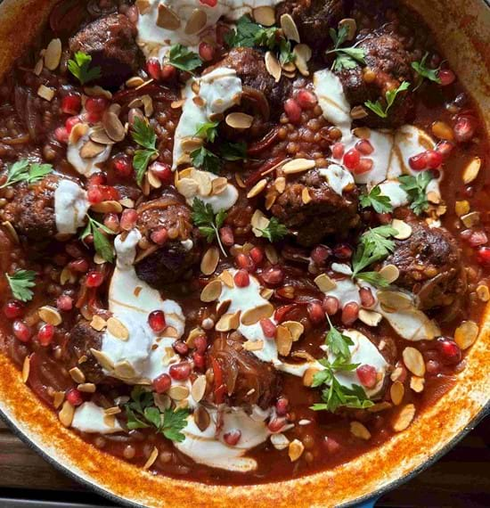 Cooked spiced beef meatballs and giant couscous in a serving dish. Drizzled with yogurt and decorated with pomegranate seeds